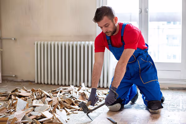 A contractor lifting old flooring, with construction debris still piled on the floor